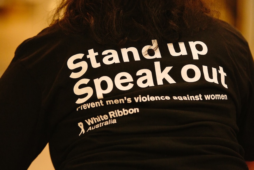 A woman wears a shirt that says "Stand up, Speak out" for the White Ribbon Foundation.