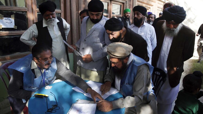 A group of men huddle around a table to cast their vote.