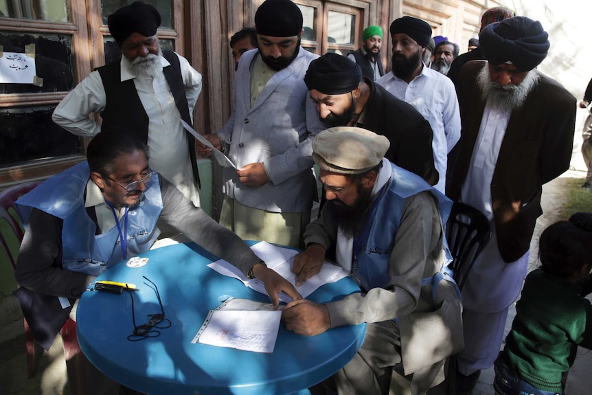 A group of men huddle around a table to cast their vote.