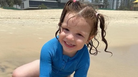 A young girl with pigtails plays on the sand at the beach.