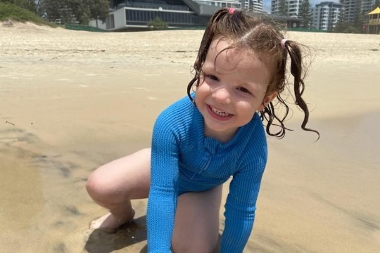 A young girl with pigtails plays on the sand at the beach.