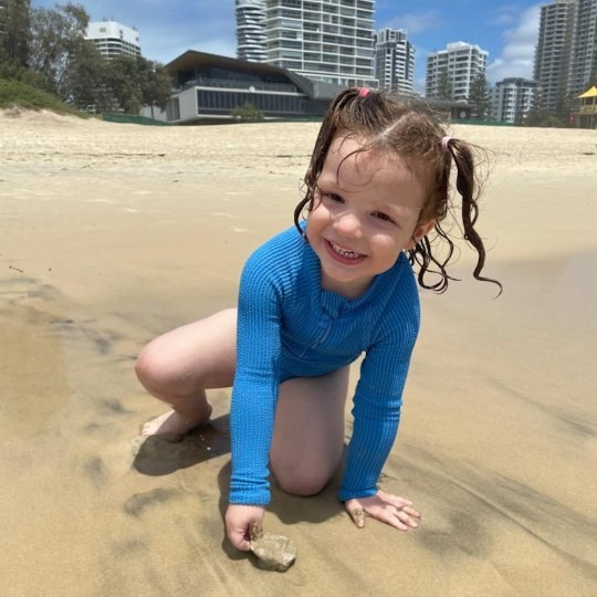 A young girl with pigtails plays on the sand at the beach.