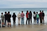 A line of people stand against the ocean backdrop.
