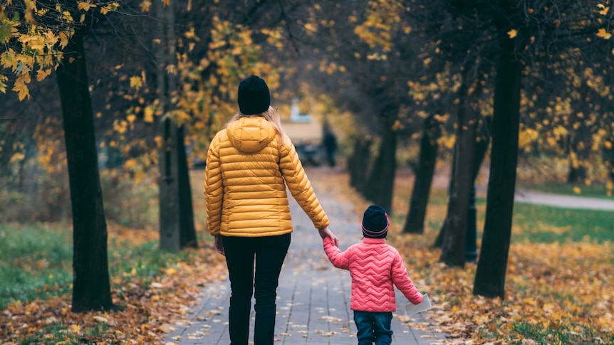 A woman and child wearing warm colourful jackets an stand on an Autumnal path.