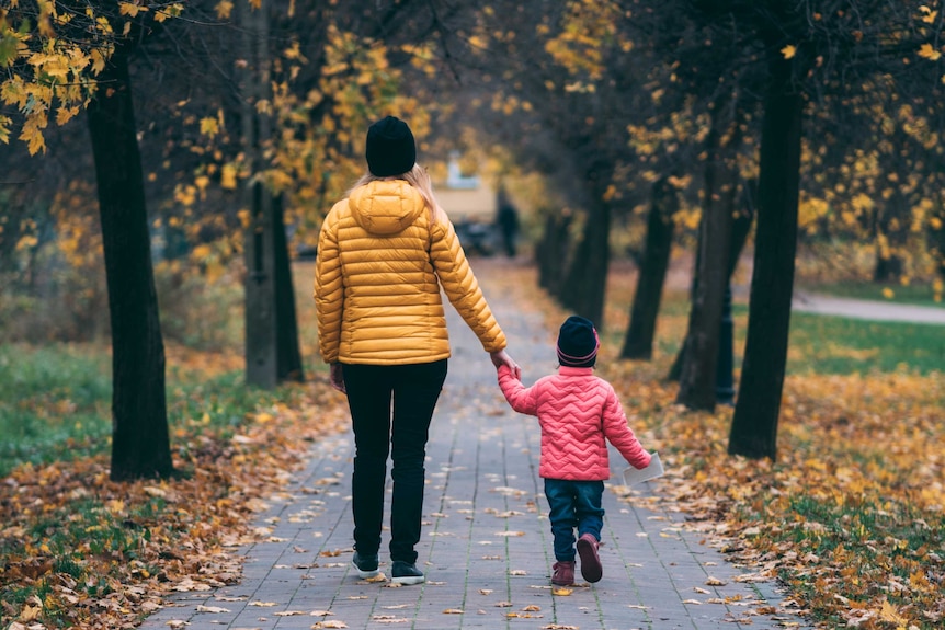 A woman and child wearing warm colourful jackets an stand on an Autumnal path.