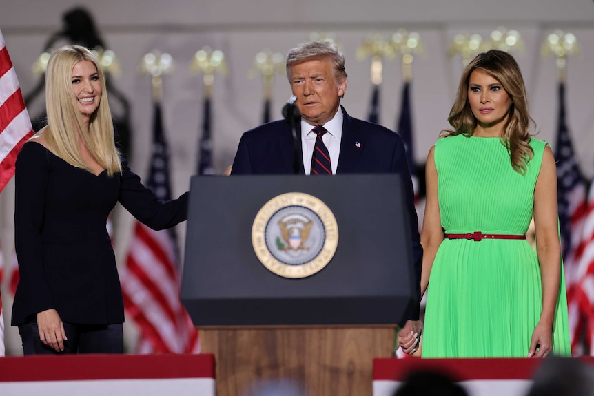 President donald trump stands behind a lectern with his daughter and wife either side of him
