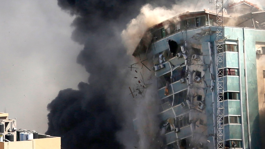 The side of a building begins to collapse as smoke bellows all around it.