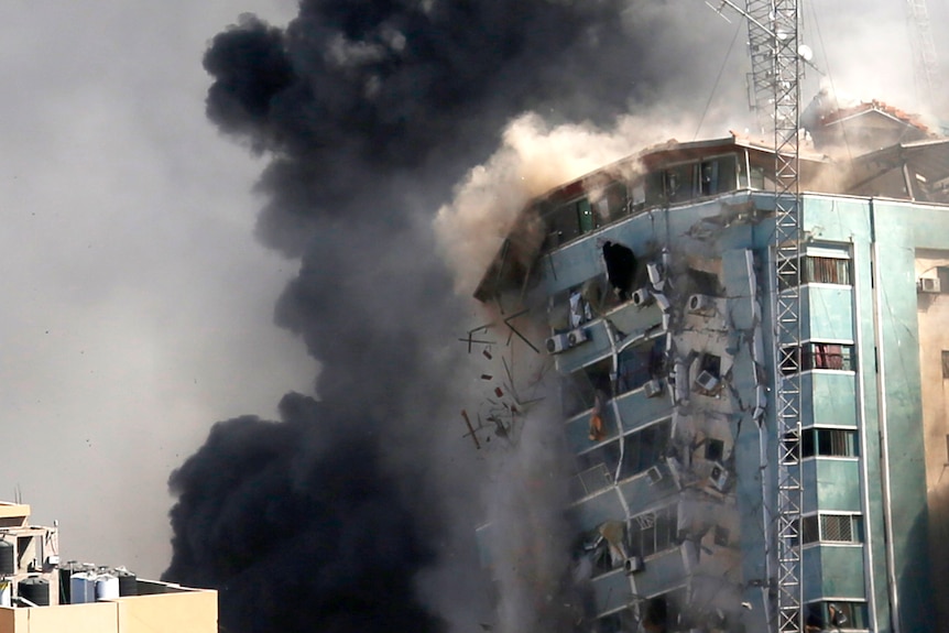 The side of a building begins to collapse as smoke bellows all around it.