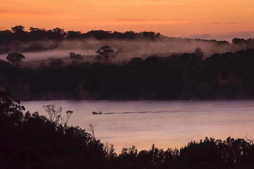 A boat on a lake at dawn with fog rising from the land