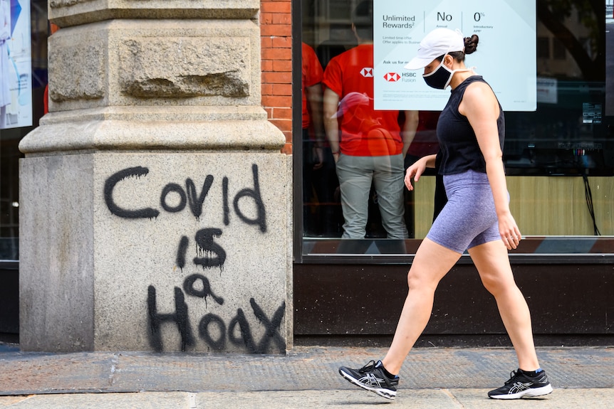 A woman walks past graffiti saying 'COVID is a hoax.'