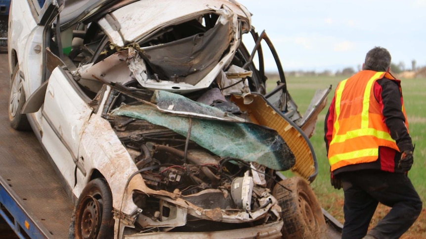 A crumpled white car being loaded onto a tow truck.