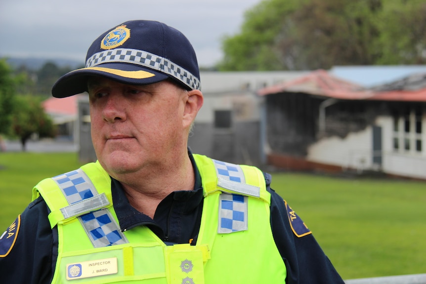 A man wearing a police uniform and cap in front of a fire damaged building