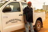 A man with glasses and a bandanna stands in front of a white ute.