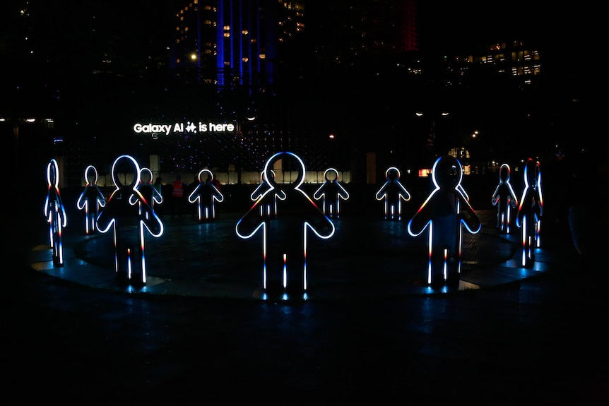 An outdoor park at night with human silhouettes lit up holding hands.