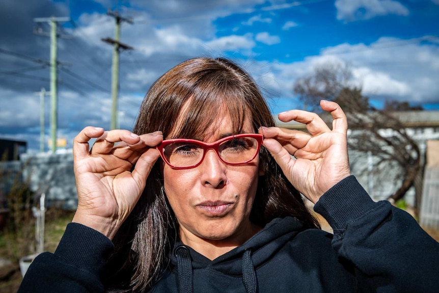 Sandy adjusts her glasses while looking into the camera