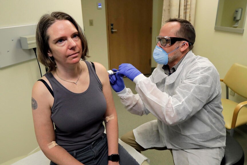 Jennifer Haller gets an injection from a man dressed in a gown and wearing a face mask.