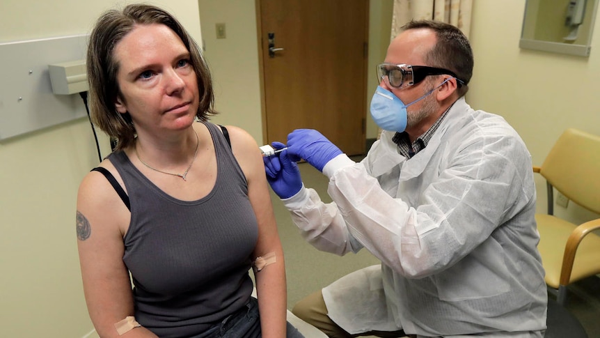 Jennifer Haller gets an injection from a man dressed in a gown and wearing a face mask.