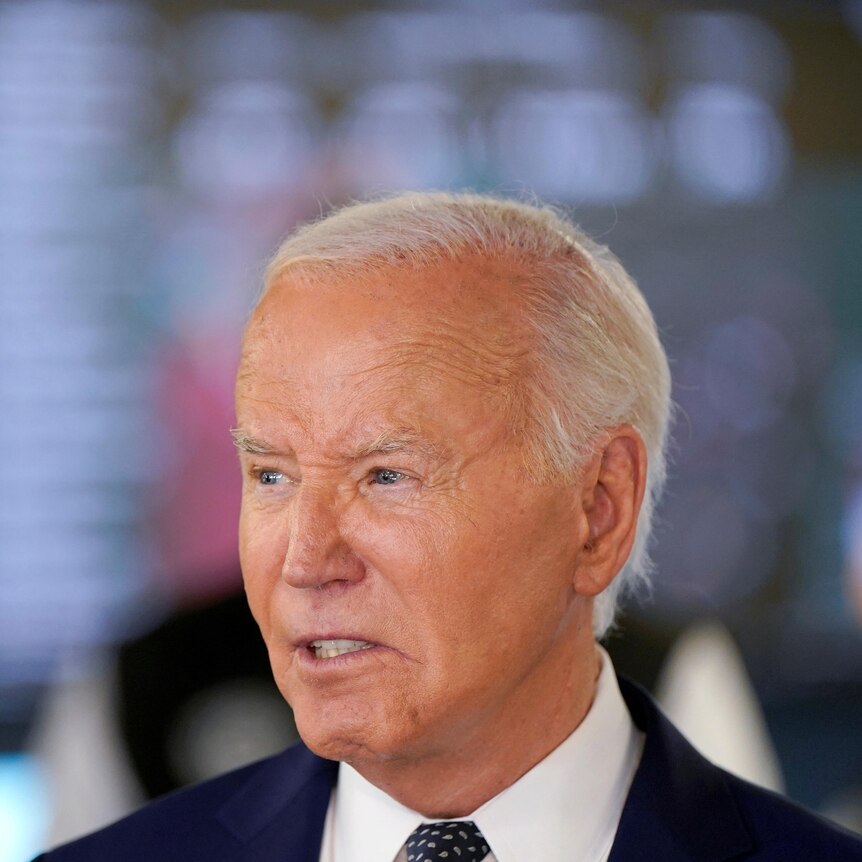 A close-up of Joe Biden with screens behind him.
