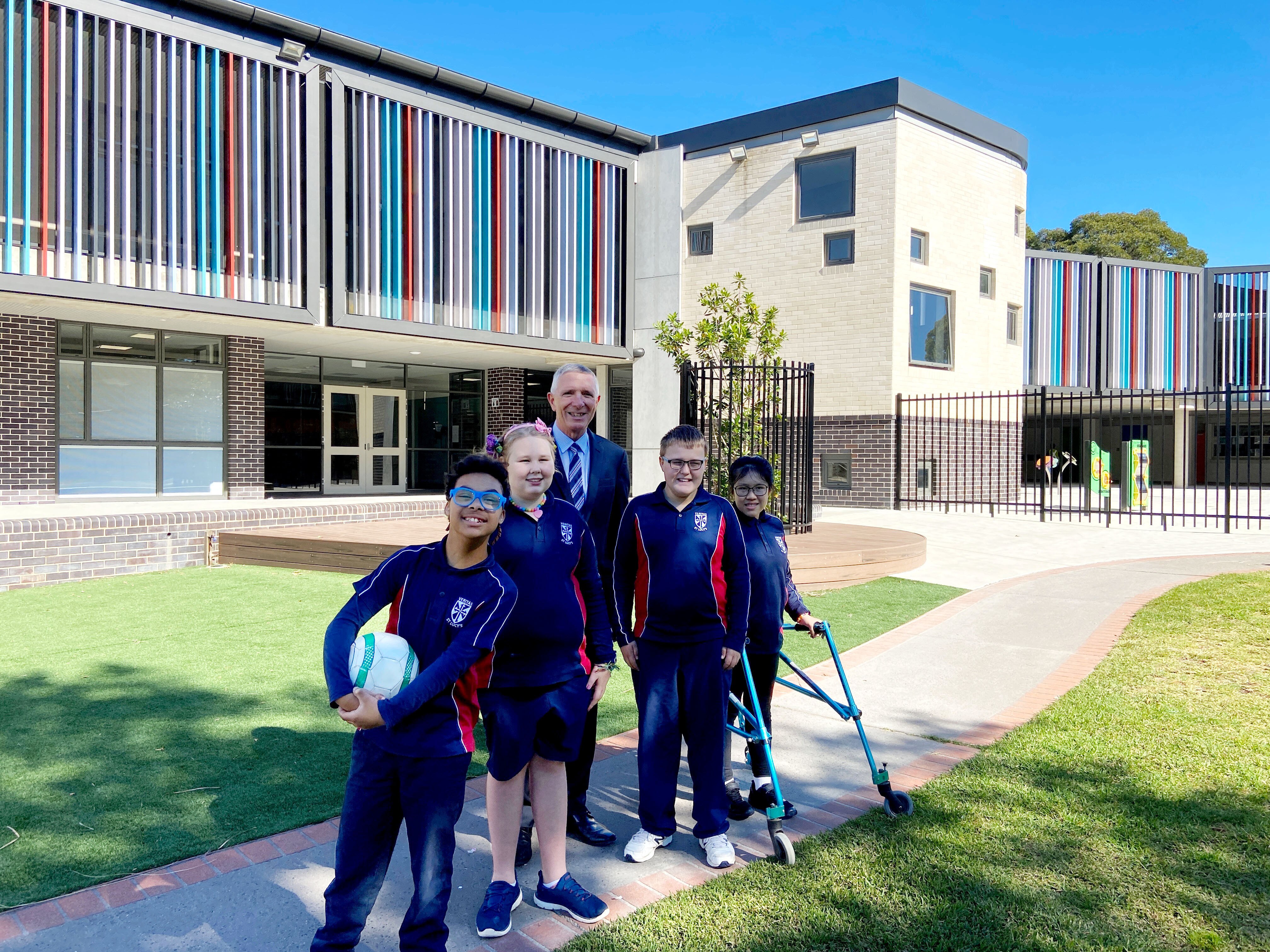A man standing in front of a school with four smiling children.
