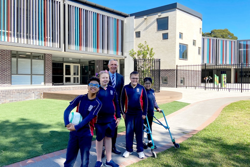 A man standing in front of a school with four smiling children.