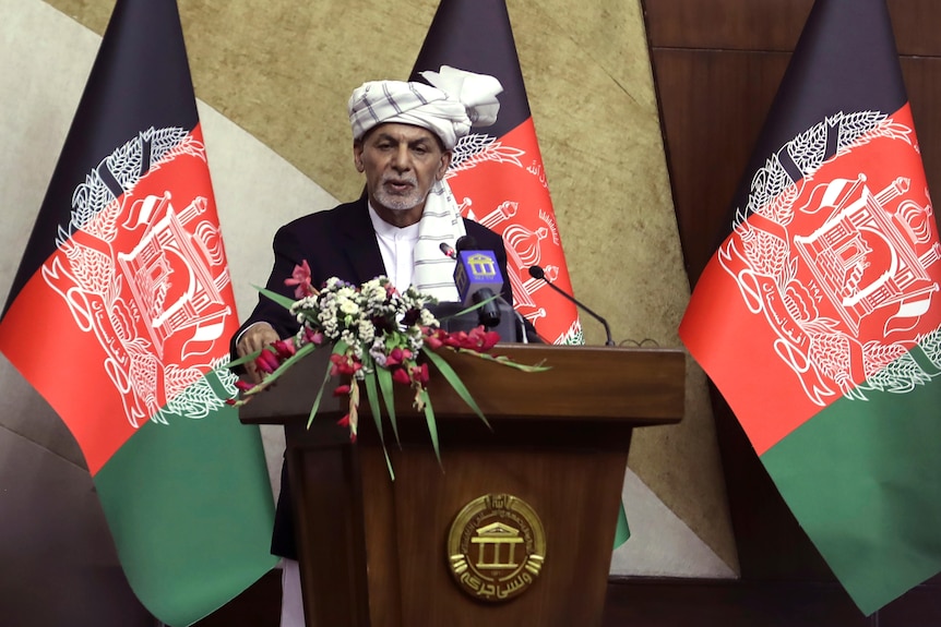 Afghan President Ashraf Ghani stands at a podium with Afghan flags behind him, speaking in parliament. 