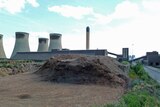 A pile of woodchips in front of a power station.