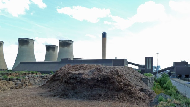 A pile of woodchips in front of a power station.