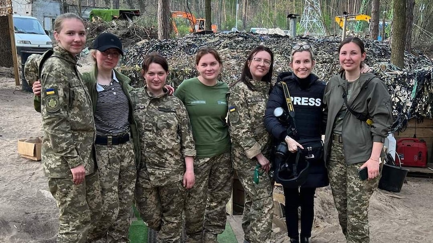 Six women in army attire and one press photographer standing together.