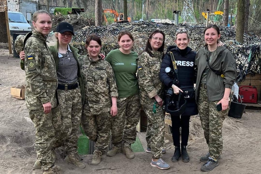 Six women in army attire and one press photographer standing together.