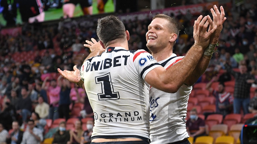 A pair of Sydney Roosters teammates hug as the player on the right smiles after kicking a goal. 