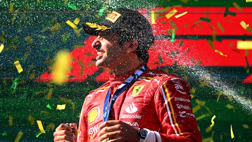Carlos Sainz standing on the podium, being sprayed with wine, celebrating his victory.