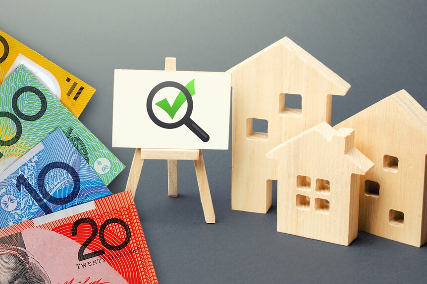 Una imagen compuesta que muestra dinero en efectivo, una marca en un letrero y figuras recortadas de madera de casas.