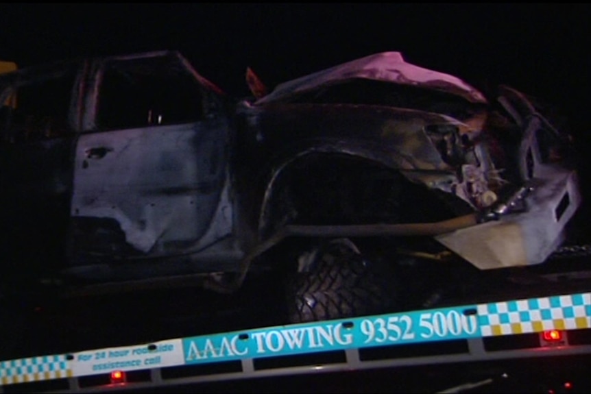 A dark photo of a badly damaged vehicle on a tow truck ramp.