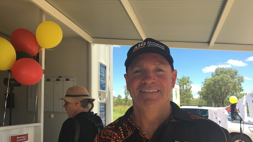 Steve Smith, wearing an AIG branded shirt and hat, smiles outside a building. There are red and yellow balloons behind him