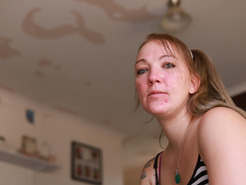 A young woman looks into the camera, with a flaking paint on the ceiling visible behind her.