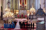 A man and a woman get married in a grand Christian church surrounded by bridesmaids and groomsmen.