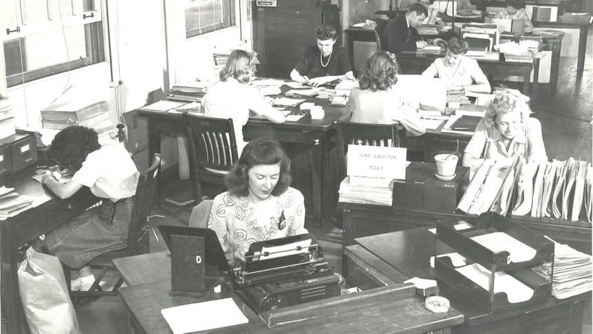 A B& W pic of women working at typewriters with piles of papers in a big hall