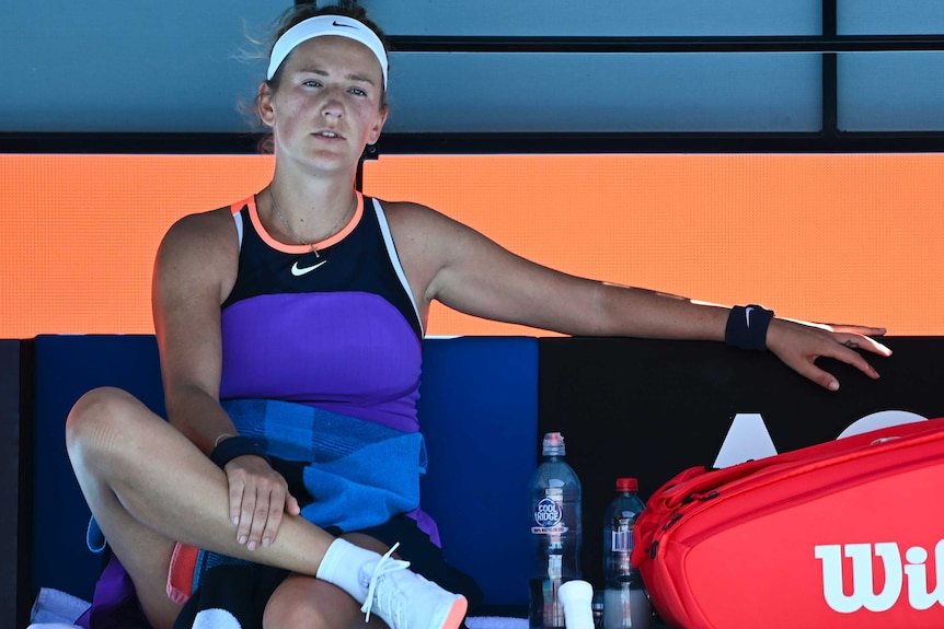 Victoria Azarenka has a tired expression while she sits cross-legged on her courtside bench