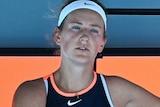 Victoria Azarenka has a tired expression while she sits cross-legged on her courtside bench