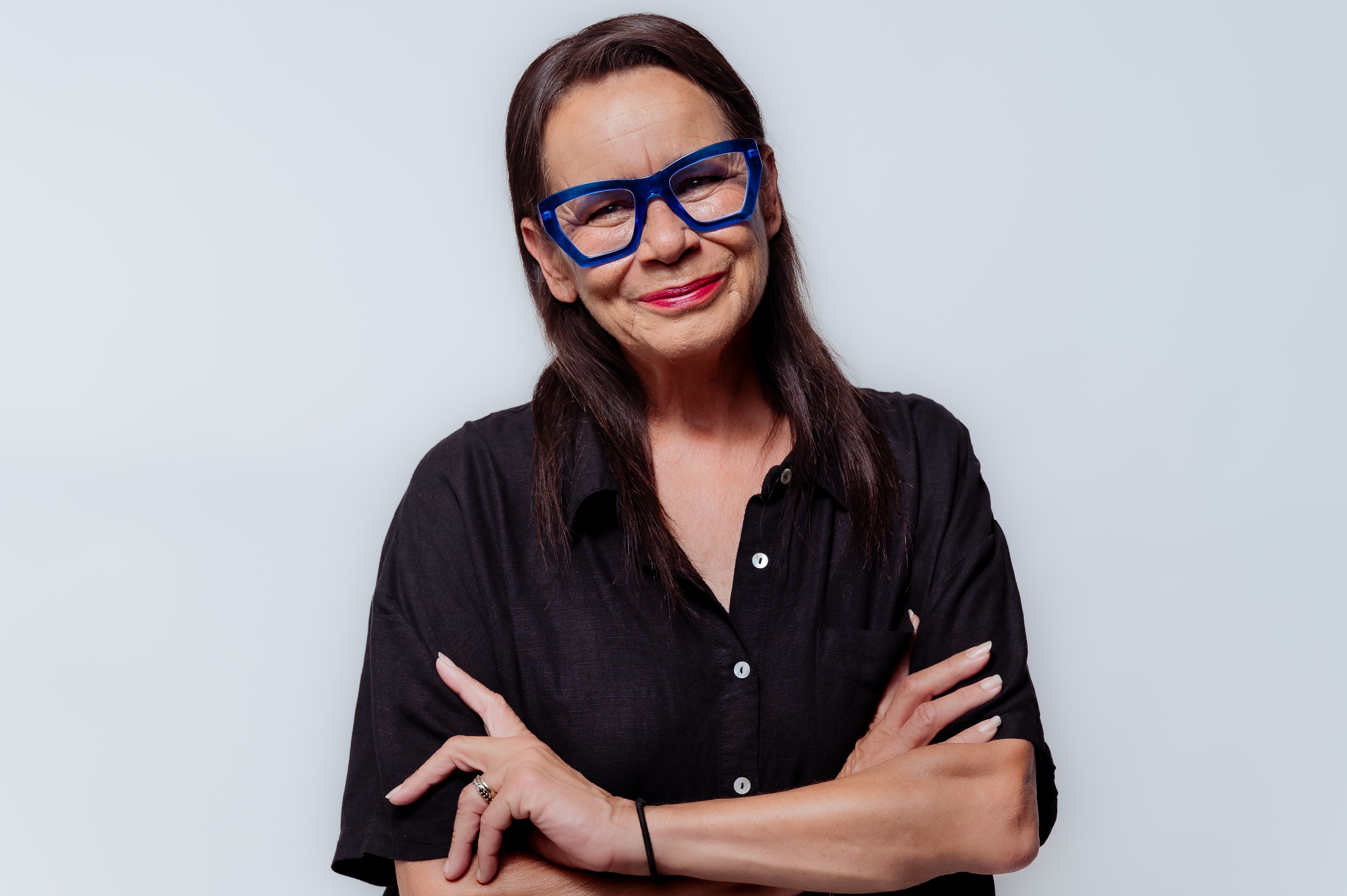 Rhoda crosses arms, wears black shirt and blue glasses