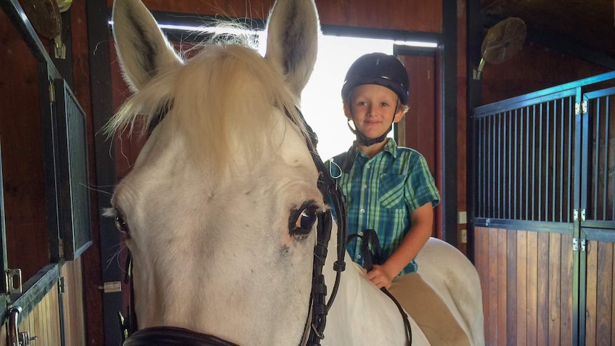 Young boy sitting on his white pony.