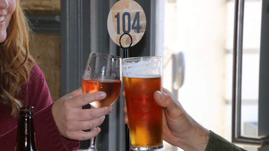 A couple gently clink their wine and beer glasses together at a pub table.