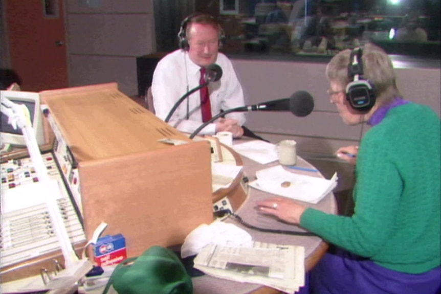 a woman in a green jumper is interviewing a man in a suit in a radio studio