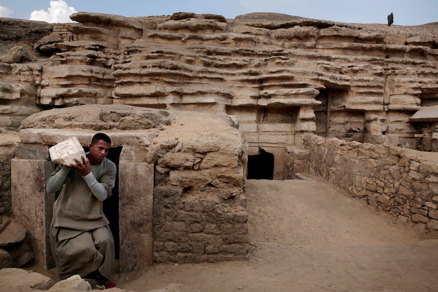 A worker carries an artefact out of a tomb, at an ancient necropolis near Egypt's famed pyramids in Saqqara.