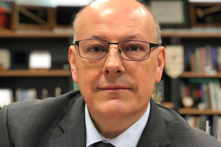 James Ogloff, wearing slim black spectacles and a charcoal suit, in front of a bookshelf