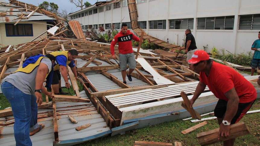 Wide shot of men cleaning up the debris of a roof.