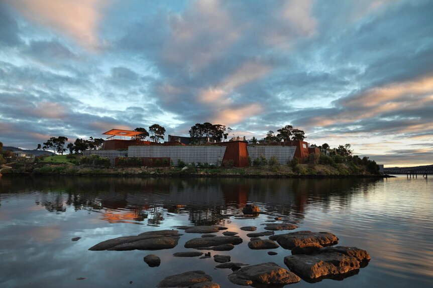 The Museum of Old and New Art set against a pink and blue sky, reflected in water surrounding its island location.
