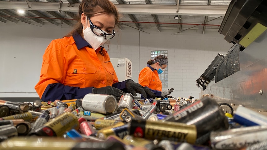 workers in high vis with a conveyer of small batteries