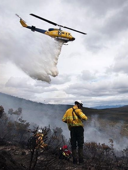 Helicopter waterbombing a bushfire, watched by ground crew.