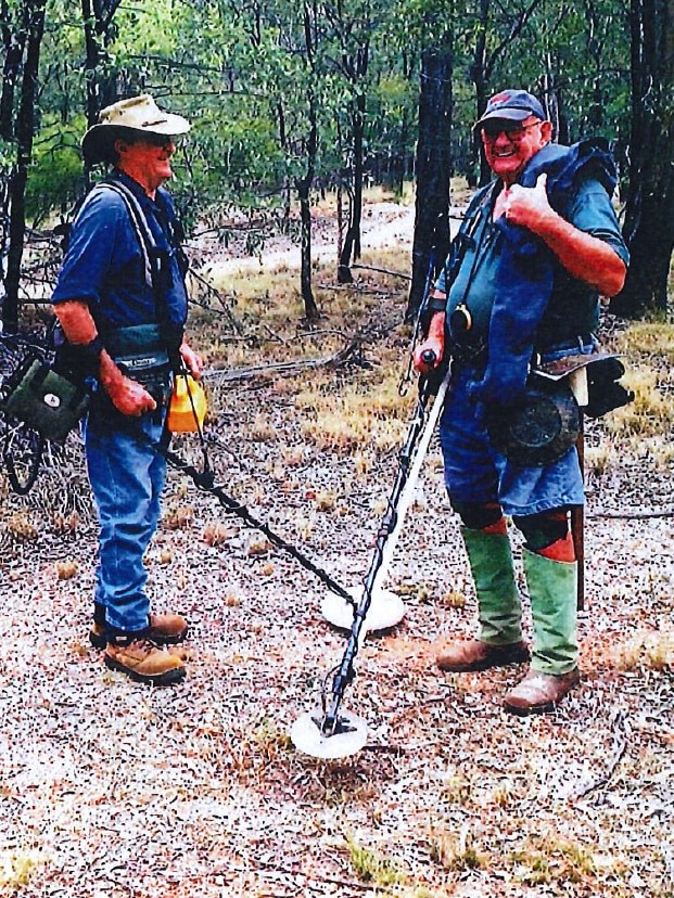 Paul and John stand in the bush with their metal detectors.